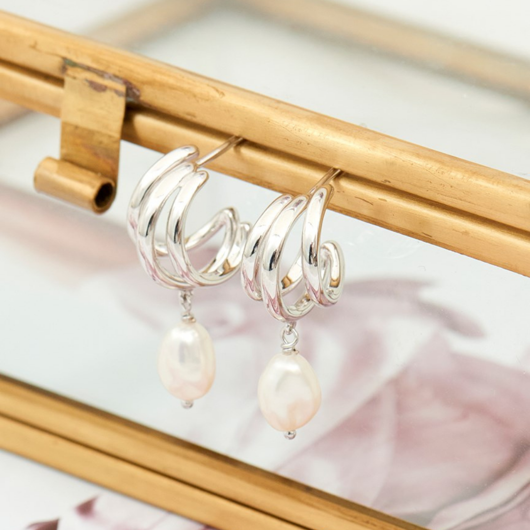 A photo of a pair of Ania haie pearl earrings sitting on a glass jewellery box
