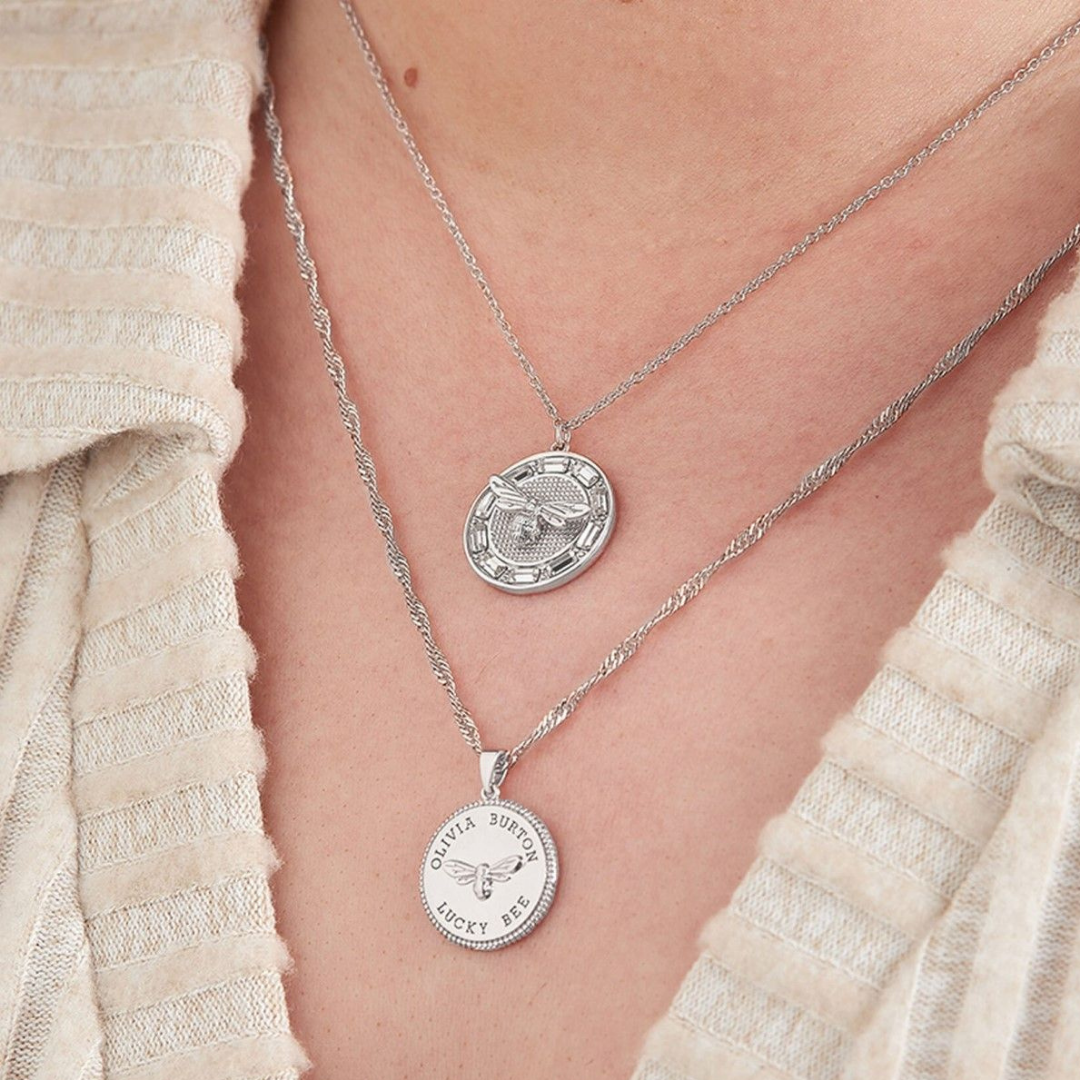 Photograph of a woman's neckline, she is wearing two silver coin necklaces by Olivia Burton