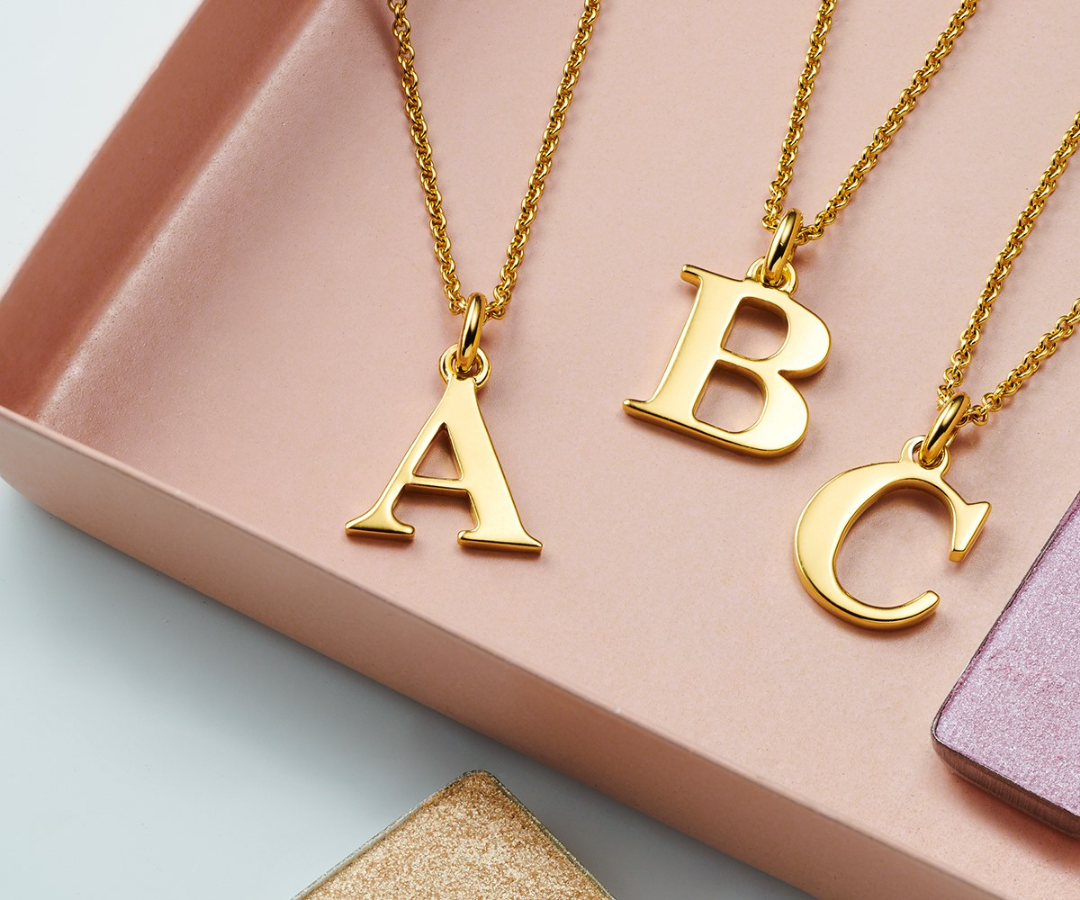 Photograph of the initials 'A', 'B', 'C', in gold on gold chains for a feature about personalised jewellery