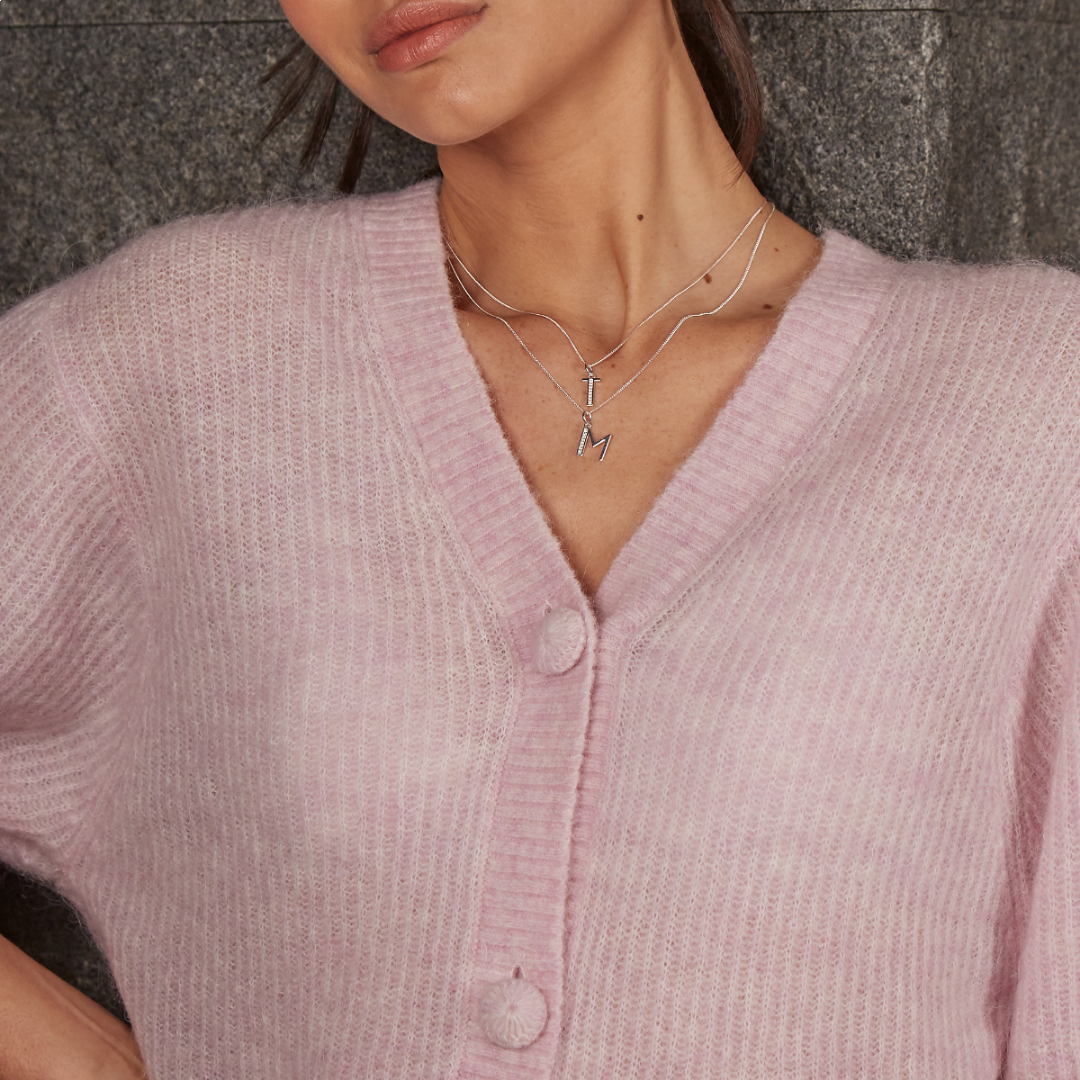 Photograph of a woman wearing a pink cardigan and a silver necklace with several initials