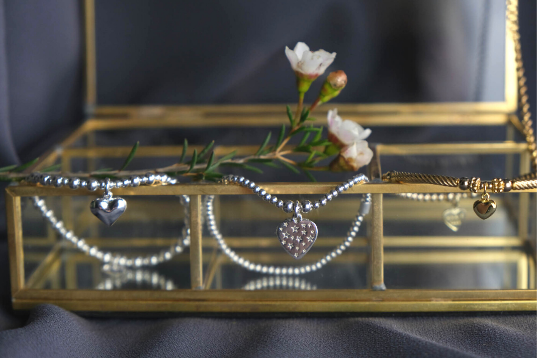 Photograph of three bracelets by Annie Haak all with heart charms, draped over a gold and glass jewellery box