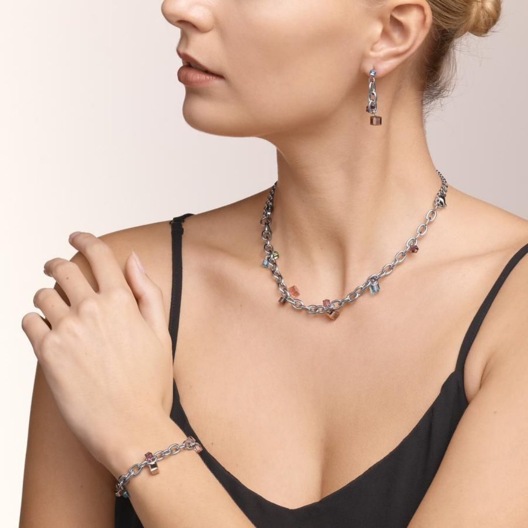 Photograph of a woman wearing a chunky chain necklace and bracelet with colourful gemstones. The jewellery is made by Coeur de lion and is reflective of new trends in jewellery from the AW catwalks