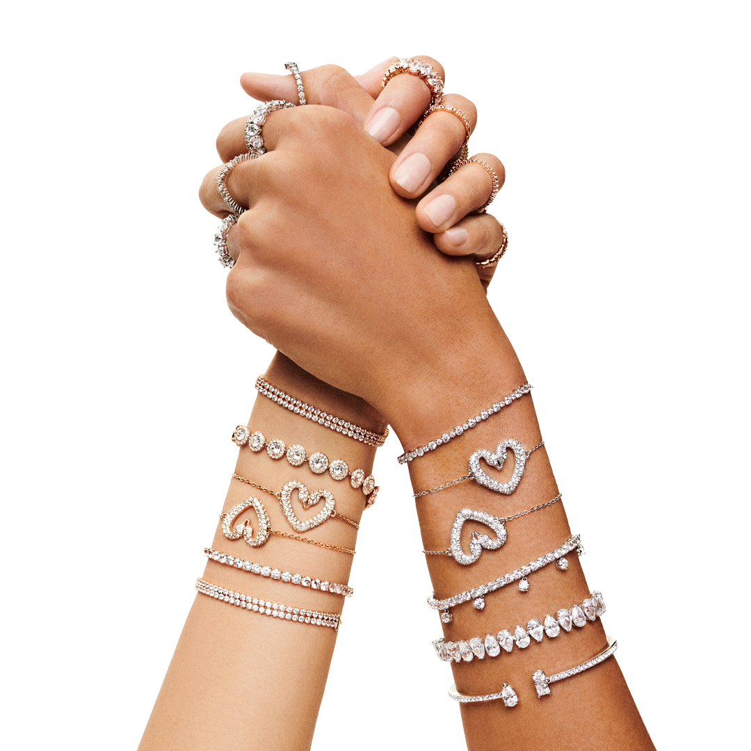 Photograph of two hands clasped, each hand's wrist is adorned with several bracelets by swarovski
