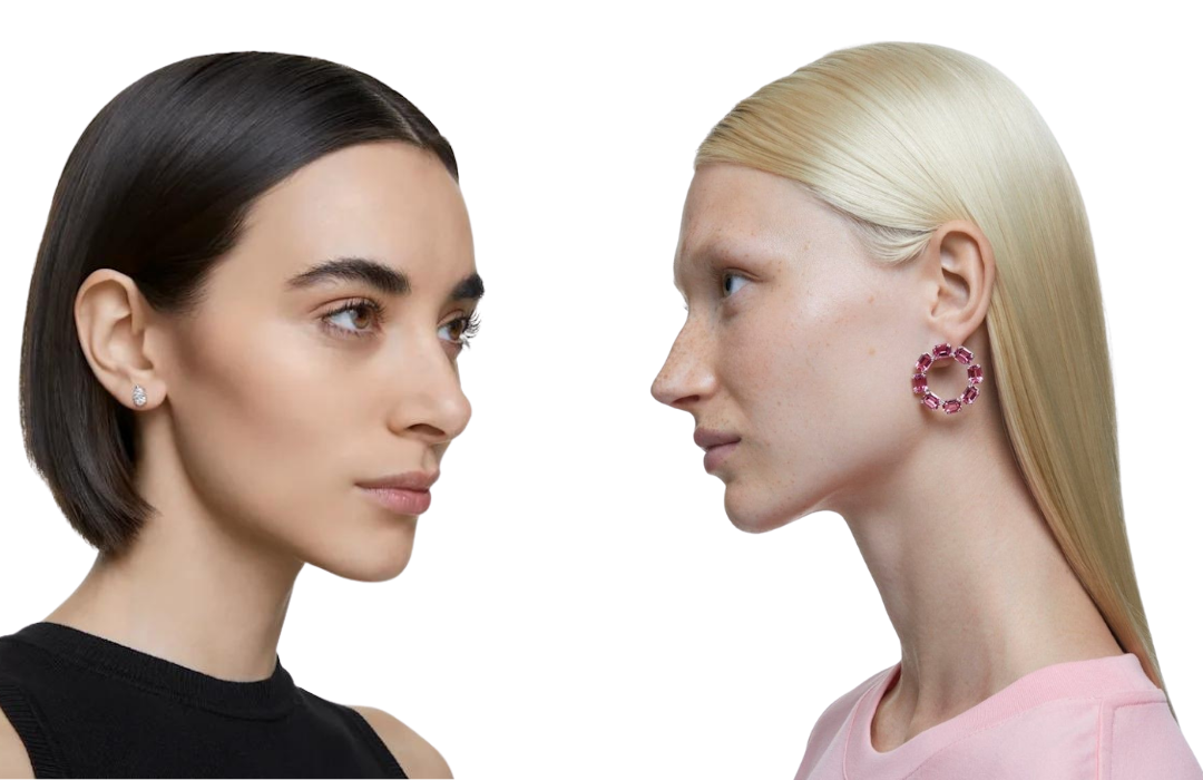 Photograph of two women. One wears single white crystal stud earrings and the other pink crystal hoops, both made by swarovski